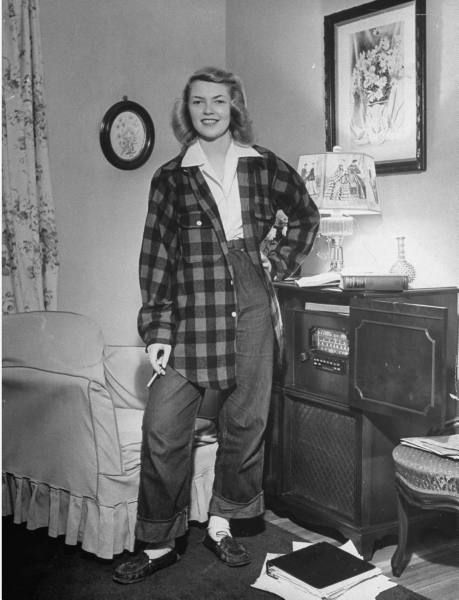 1940s vintage image of a young girl in a plaid oversize jacket, jeans and smoking in her livingroom beside the radio. 