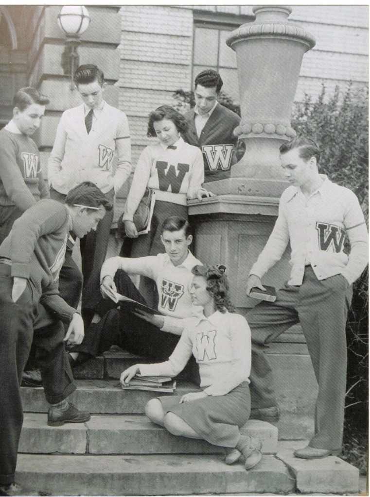 1950s vintage photo of students in their letterman sweaters po;sing together outside of school. 