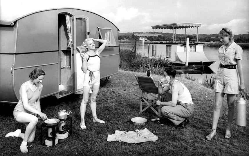 1930s vintage camping image of women and men in swimsuits and summer fashions outside of their camper. 