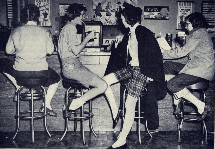 1952 malt shop image featuring teenage girls in 1950s fashiosn hanging out at the counter.