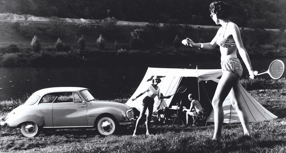 1950s vintage photo of two wome playing badmonton outside of a tent by their car in 1950s summer fashions. 