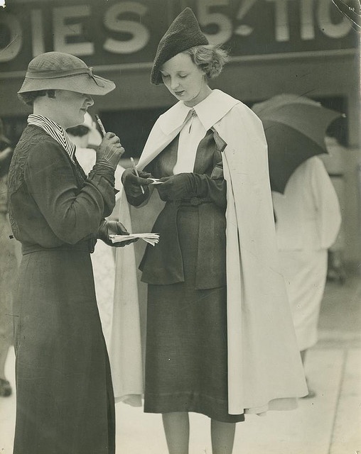 1930s racetrack fashion- 1930s vintage photo of two woman in 1930s fashions writing down their bets at the racetrack. 