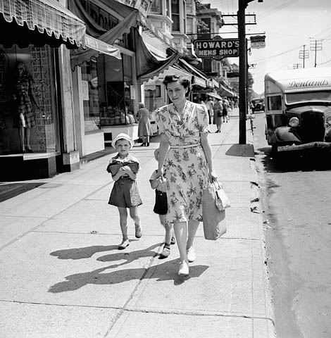 1940s vintage photo of a Toronto street in 1943 featuring a woman in a 1940s dress walking down the street with her child in tow. 