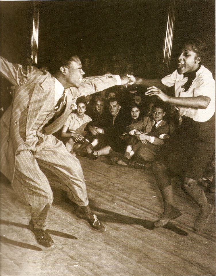 1940s vintage photo of lindy hoppers at the Savoy Ballroom with white and Black dancers watching off to the side. 