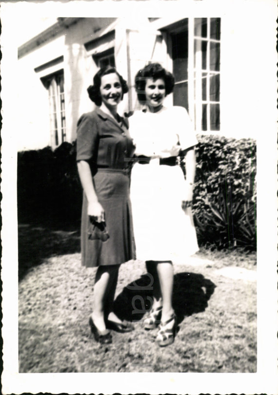 1940s vintage image of 2 women in front of house the one woman is holding her eyeglasses. 