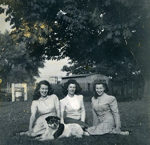 1940s vintage photo of 3 women with 1940s hairstyles and 1940s fashions sitting on the grass for a photo. 