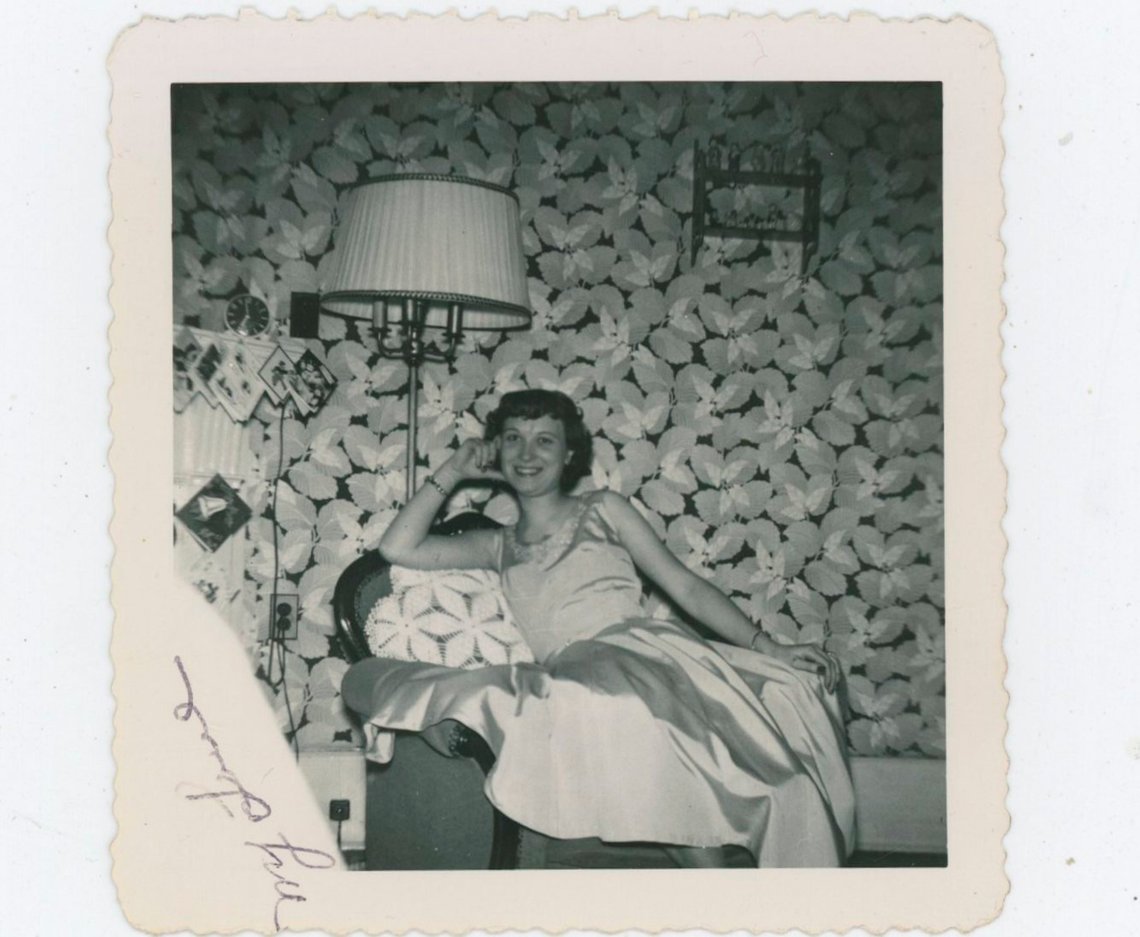 1950s Vintage Photo of a young woman posing in front of a wall with wallpaper on it. 