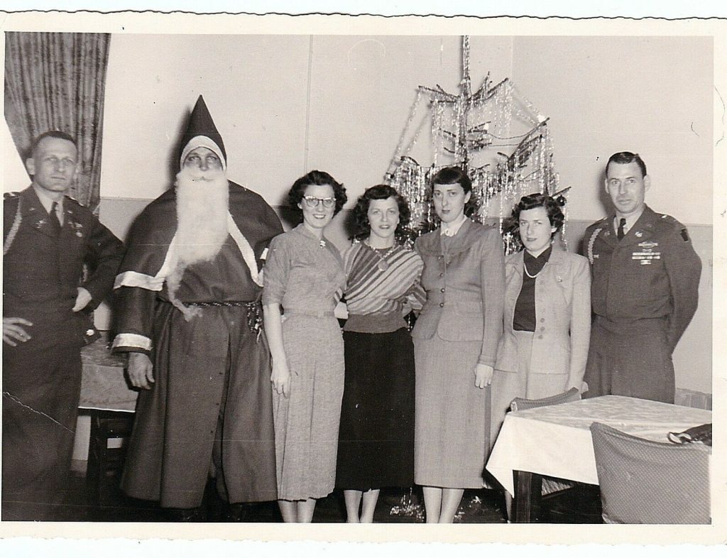 1950s vintage photo of the work Christmas Party featuring Papa Noel (aka Santa Claus), stylish women and 2 men in uniform. Great 1950s fashions on our ladies in the middle (love the striped sweater).