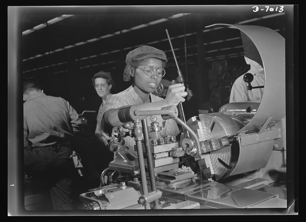 1940s photo of a young Black woman working on a machine in a factory. According to the Library of Congress, “Plant foremen point to 20-year-old Annie Tabor as one of their best lathe operators, despite her lack of previous industrial experience.”
