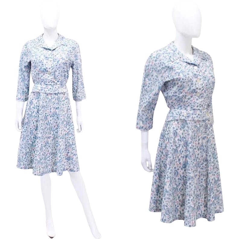 1950s Fashion: 1950's professional construction from the Nathalie Nicoli of California label. This darling summer suit is made from a lightweight cotton fabric featuring a whimsical floral print in pale blue with pops of pink. The set features a crop "jacket" top with glove length sleeves, notched lapel collar, and a perfect nip at the waist. The skirt has a nipped waist, nice full A-line cut, and a flirty youthful knee length.