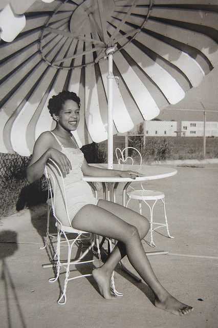 1950s photo of a young Black woman taking a break by the pool under an incredibly cool patio umberalla in Greenwood, Mississippi.