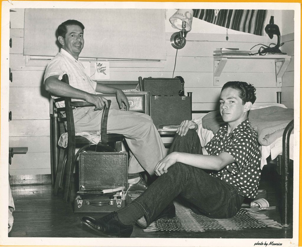 1950s vintage photo of two young college men listening to the record player in their dorm room in 1951 at palm beach junior college. They are wearing 1950s fashions and 1950s hairstyles for men. 