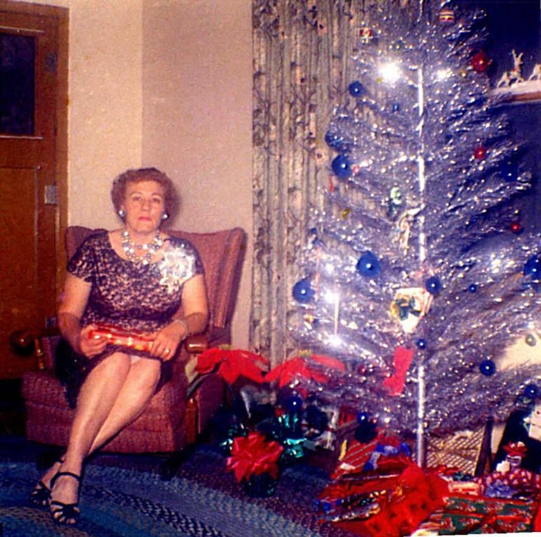 1960s Vintage Photo of a woman sitting beside an aluminum Christmas Tree wearing a Christmas Corsage and a 1960s Dress. 