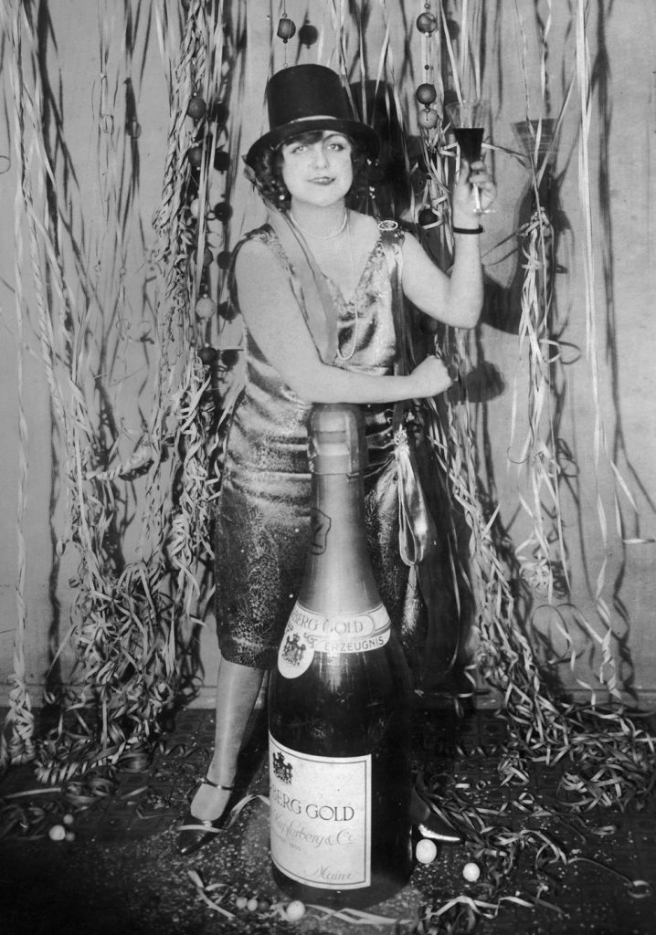 circa 1925:  A woman at a New Year's Eve party leans on an oversized bottle of champagne while making a toast, Germany.  (Photo by Hulton Archive/Getty Images)