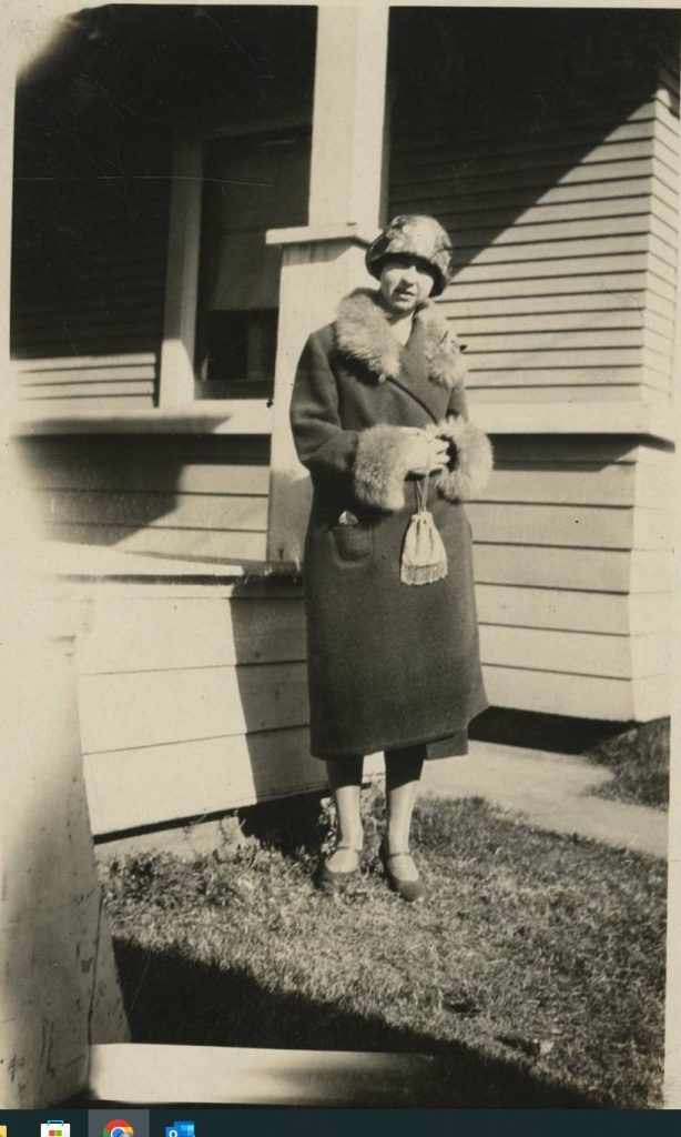 1920s vintage photo of a woman in a 1920s winter fur coat, 1920s hat, 1920s purse posing for a photo in front of her house. Fantastic 1920s style!