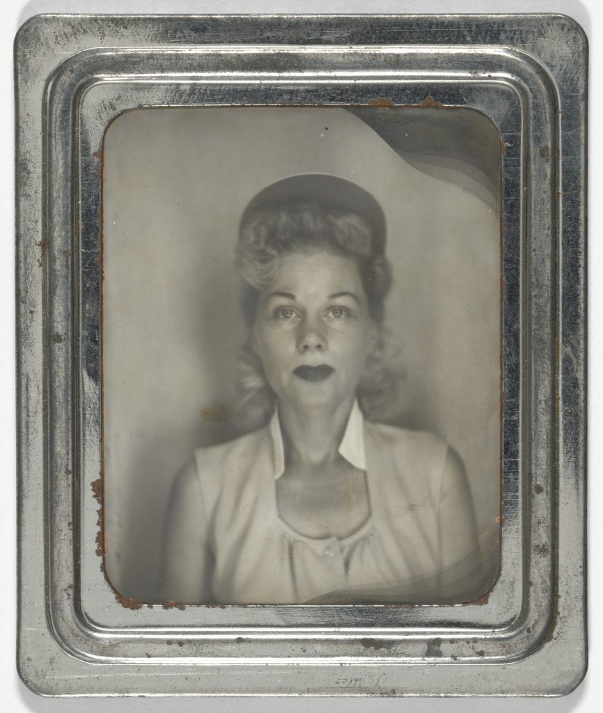 1940s vintage photo of a 1940s woman baseball player (league of their own) wearing red lipstick, a baseball cap and a 1940s hairstyle as she poses for a photo booth photo. 