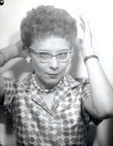 1950s photo booth image of a woman in a polkadot dress and cat eye glasses and curly hair