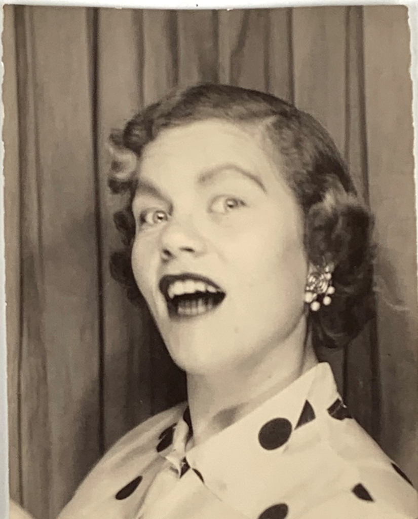 1950s vintage photo booth image of a young woman in a polkdot shirt and clip on earrings posing goofy.