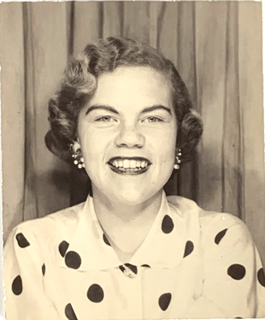 1950s vintage photo of a young woman posing in a photo booth with a 1950s hairstyle, red lips, 1950s accessories. 