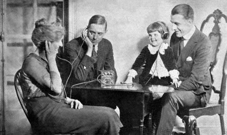 1920s vntage photo: A family listening to the first broadcasts around 1920 with a crystal radio. The crystal radio, a legacy from the pre-broadcast era, could not power a loudspeaker so the family must share earphones