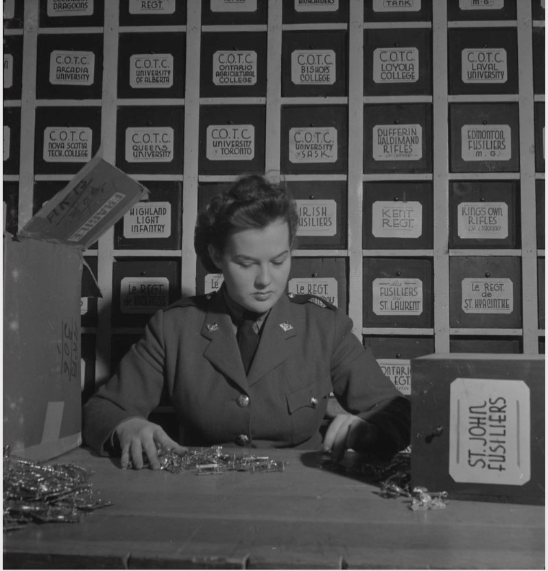 1940s vintage photo of a Canadian Woman in Military Uniform counting pins surrounded by boxes of pins from colleges and universities in Canada.