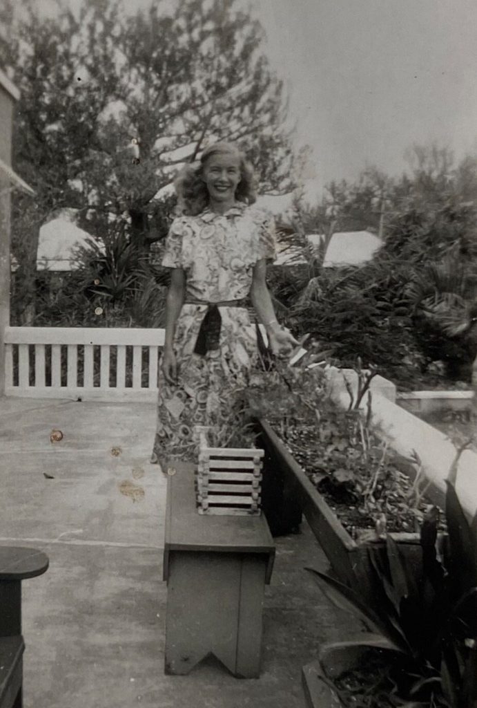 1940s vintage photo of a woman in a 1940s dress posing on a garden patio with plants beside her