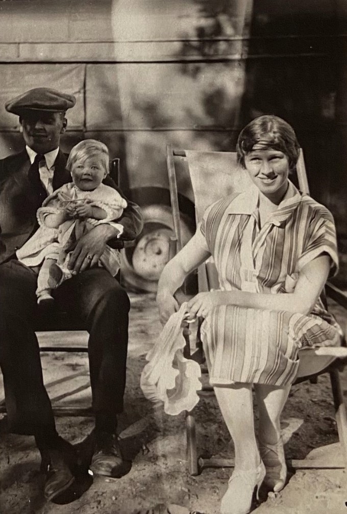 1920s vintage photo of a young 1920s mother posing with her baby and husband in a 1920s stripped dress and short 1920s hairstyle and matching hairscarf. 