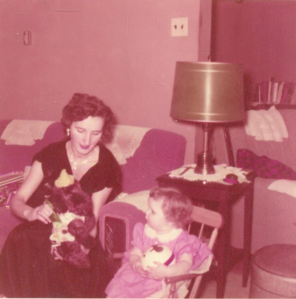 1950s vintage photo of a mother in 1957 playing with a teddy bear with her young toddler child. Mother is in a 1950s dress