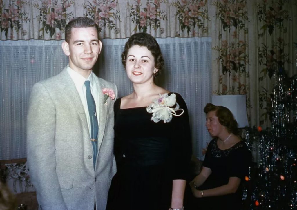 1950s vintage photo: 1950s Red Border Kodachrome of a couple in1950s fashions posing together at a Christmas Party. The woman is wearing a Christmas Corsage. 