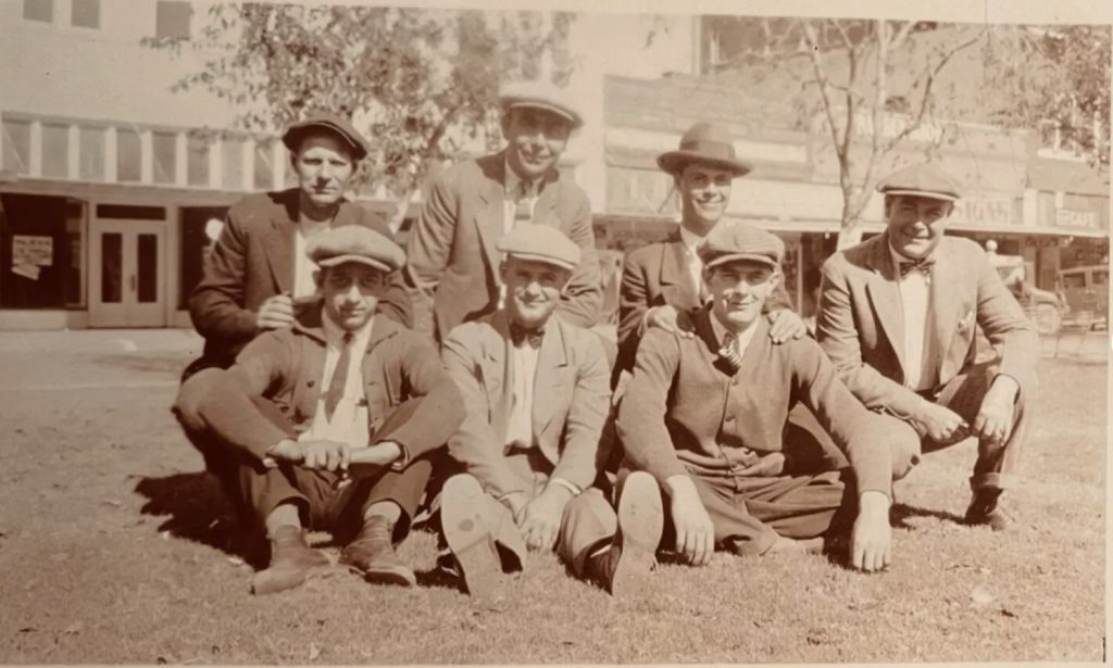 1920s photo / 1920s fashions of a group of men posing in a parkette together. Page boys, flat tops and a fedora are in the image. 