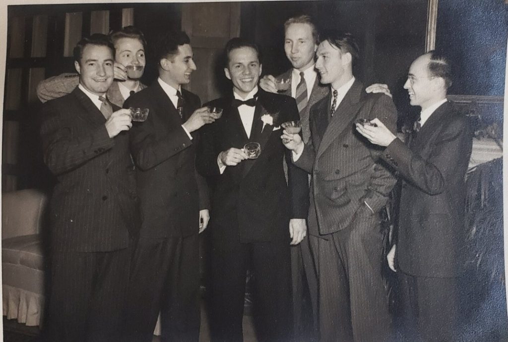 1940s vintage photo of a groom at his wedding being given a toast by his friends everyone is in suits. 1940s men's fashion.