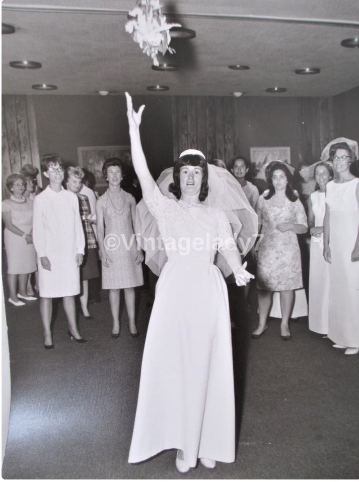 1960s vintage photo from 1966 of a Bride tossing the bouquet to her women wedding guests. 1960s fashions / 1960s wedding dress. 