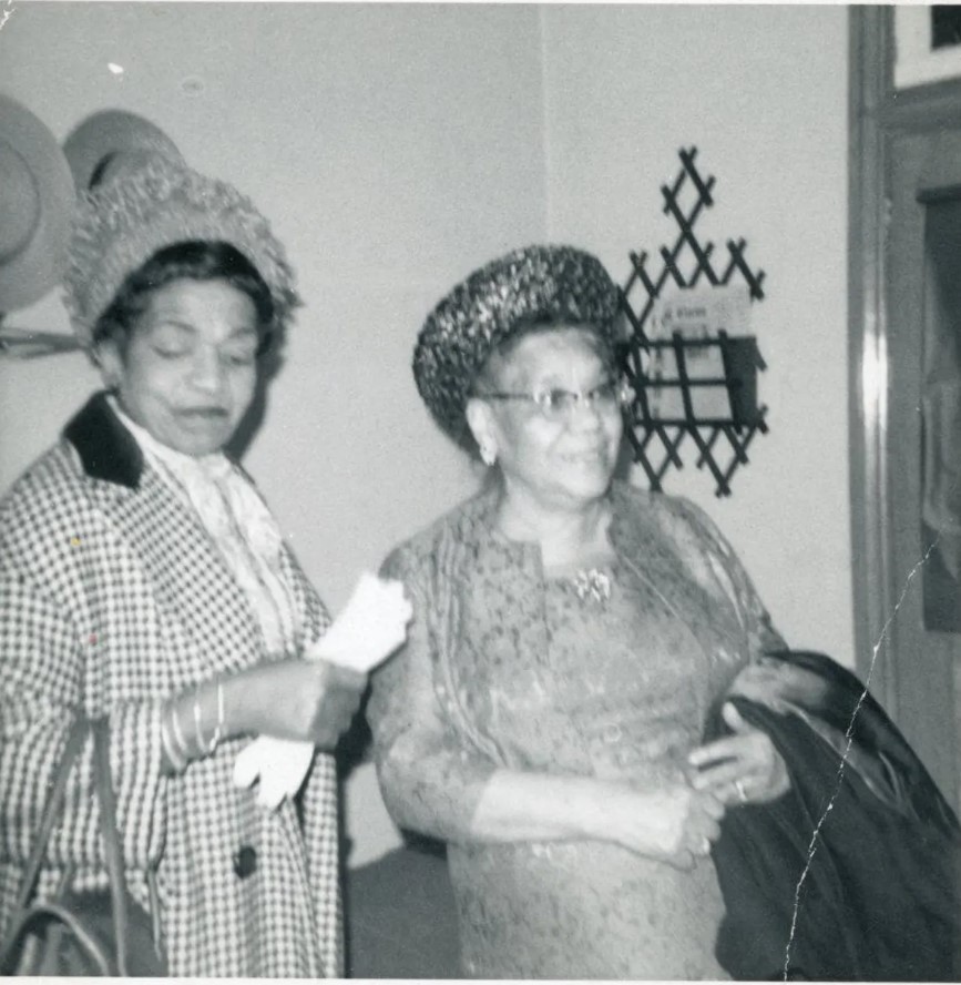 1960s vintage photo of two Black Women in their 'Sunday Best'. They are wearing 1960s hats and 1960s dresses and one lady has a houndstooth jacket. Very stylish! 