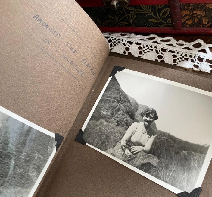 1950s vintage photo album of a couples trip to Scotland in 1955 featuring an image of a pretty woman in a plaid skirt sitting amongst the heather in Glencoe
