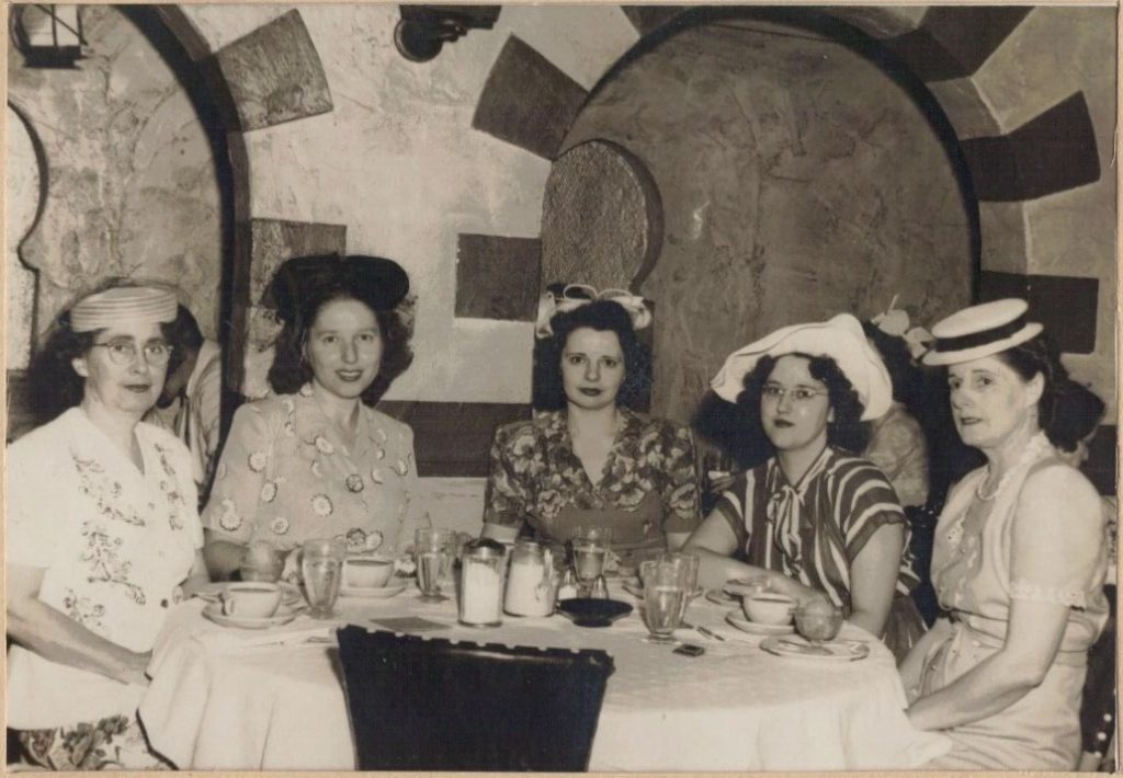 1940s photo of a group of women wearing various 1940s hats and 1940s fashions (dresses and skirts and tops) dining at 'Restaurant Madrillon' in the Washington Building in Washington D.C
